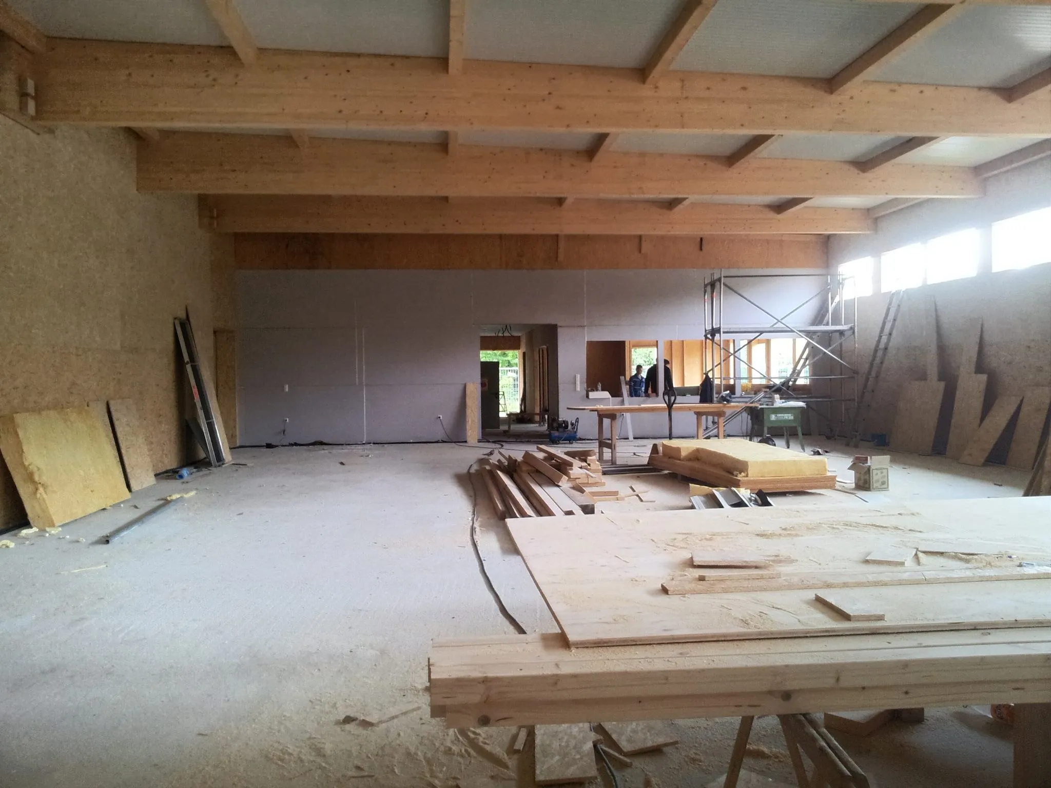 Innenansicht der Halle im Rohbau: sichtbarer Dachstuhl aus Holz, Bretter und Balken auf dem Boden